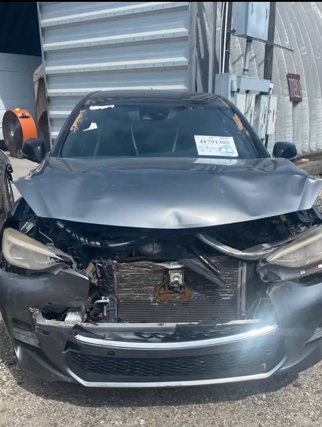 Infiniti before repair — front end crushed, hood buckled and radiator exposed